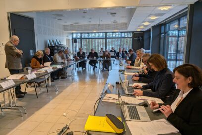La photo montre une grande salle de r&eacute;union du SIDEC du Jura. Des &eacute;lus et des agents sont assis autour de tables dispos&eacute;es en rectangle ouvert. Les participants sont install&eacute;s face &agrave; face, en train de participer &agrave; une r&eacute;union. La salle est spacieuse et lumineuse, avec un am&eacute;nagement formel typique d&rsquo;une r&eacute;union institutionnelle. - Agrandir l'image, fen&ecirc;tre modale