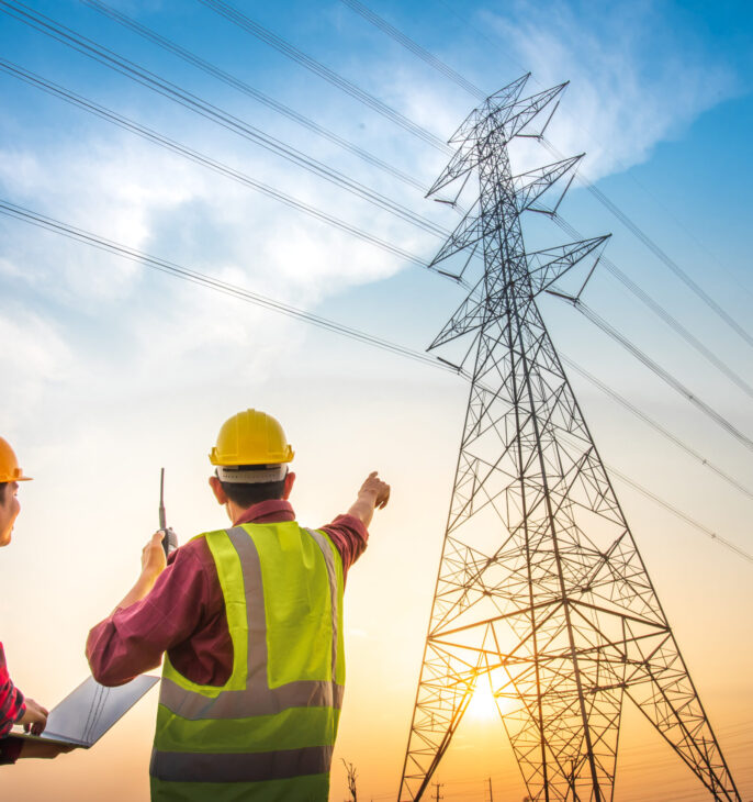 Techniciens inspectant une ligne &eacute;lectrique haute tension devant un pyl&ocirc;ne de transport d'&eacute;lectricit&eacute;.