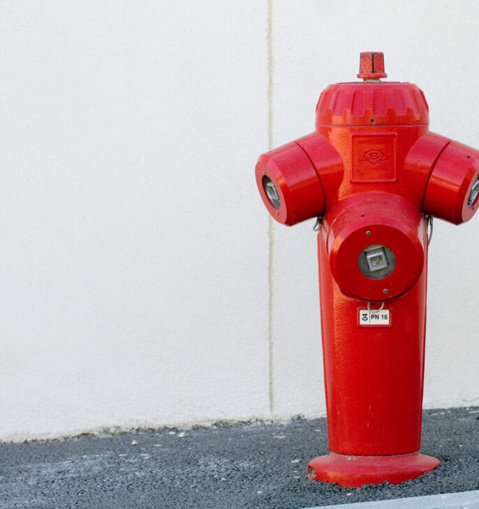 Borne incendie rouge install&eacute;e sur un trottoir devant un mur clair.