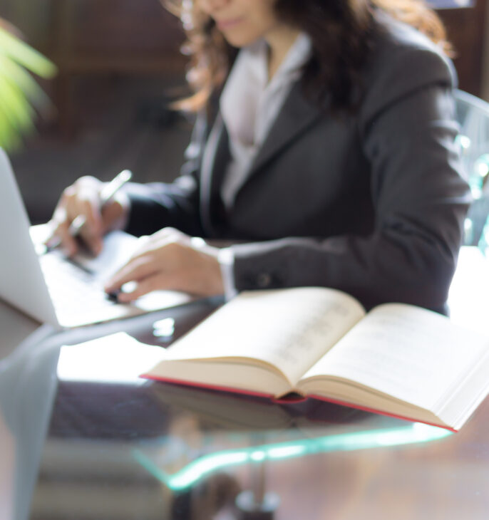 Professionnelle du droit travaillant sur un ordinateur portable avec une statue de la Justice au premier plan.